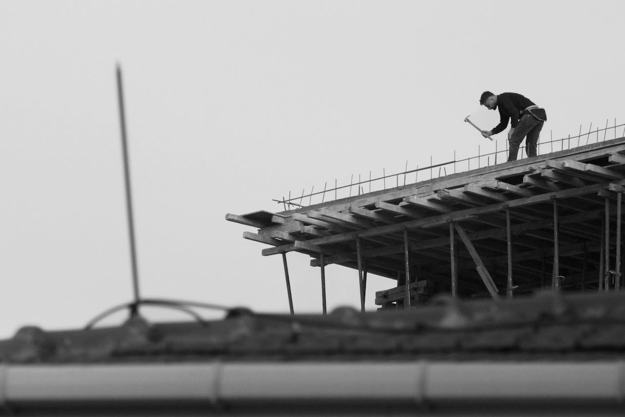 Silhouetted view of a worker building structure on a roof in monochrome.